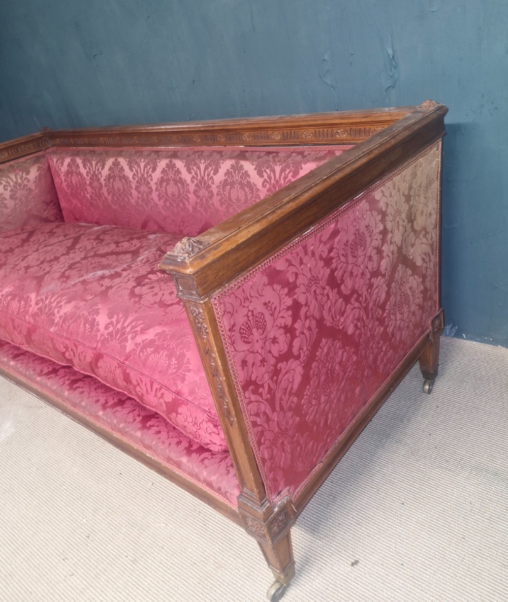 An Edwardian mahogany frame sofa upholstered in rose pink damask fabric with carved detailing along the top rail and square legs on castors. View III