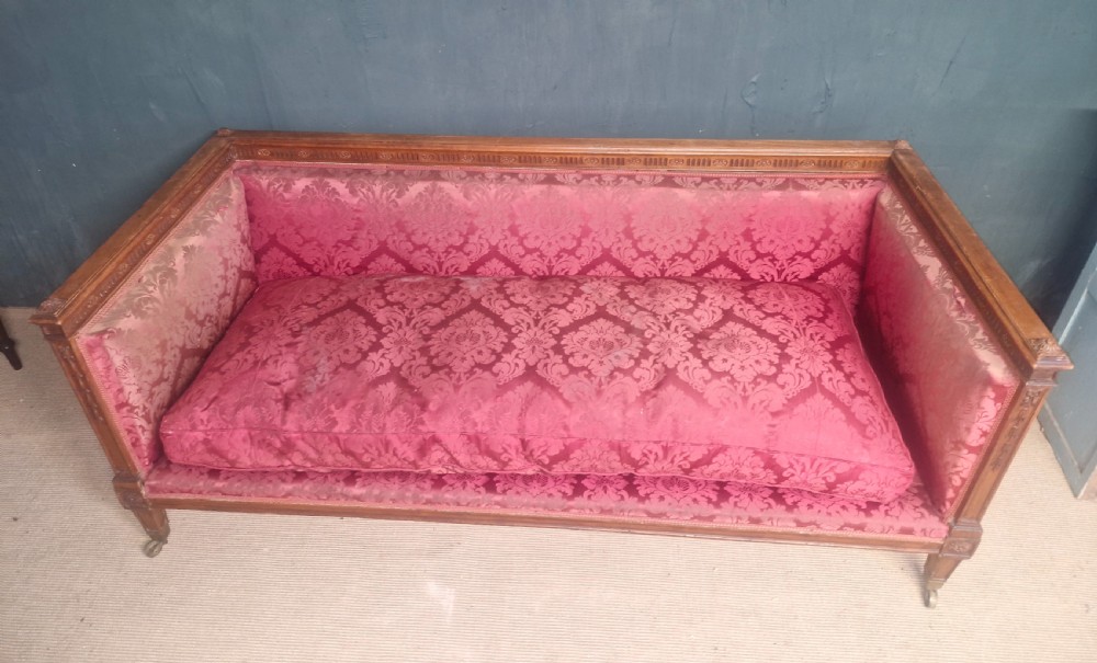 An Edwardian mahogany frame sofa upholstered in rose pink damask fabric with carved detailing along the top rail and square legs on castors. View VII