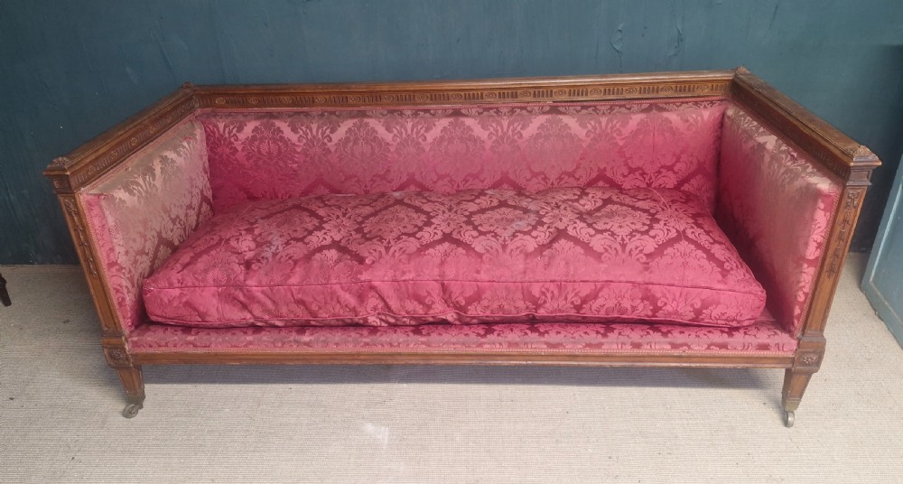 An Edwardian mahogany frame sofa upholstered in rose pink damask fabric with carved detailing along the top rail and square legs on castors. View VIII