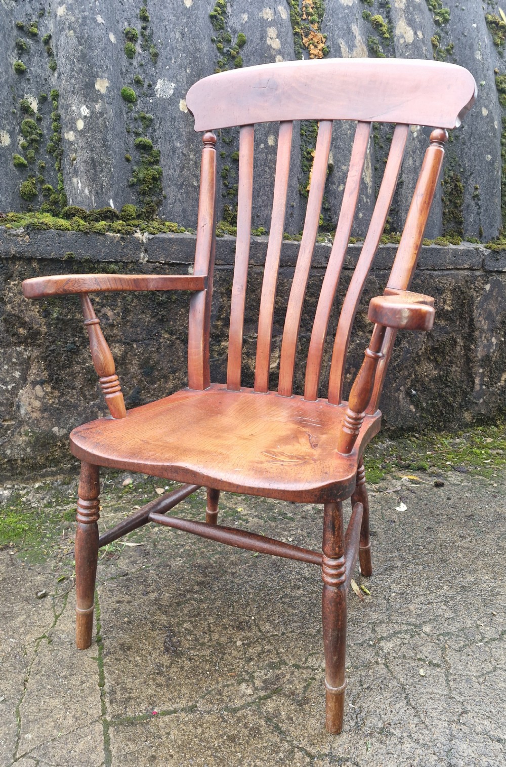 A Victorian wooden slat back Windsor armchair with turned legs, flat armrests, and a shaped saddle seat.