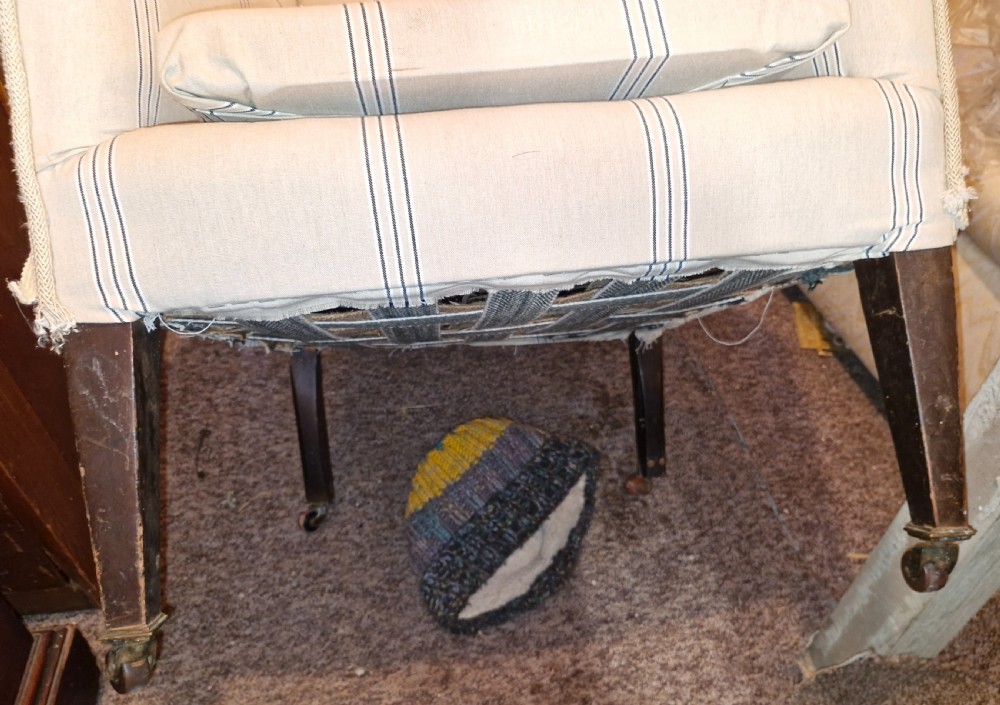 An Edwardian upholstered bedroom armchair covered in beige ticking stripe linen with tapered front legs set on brass castors. View IV