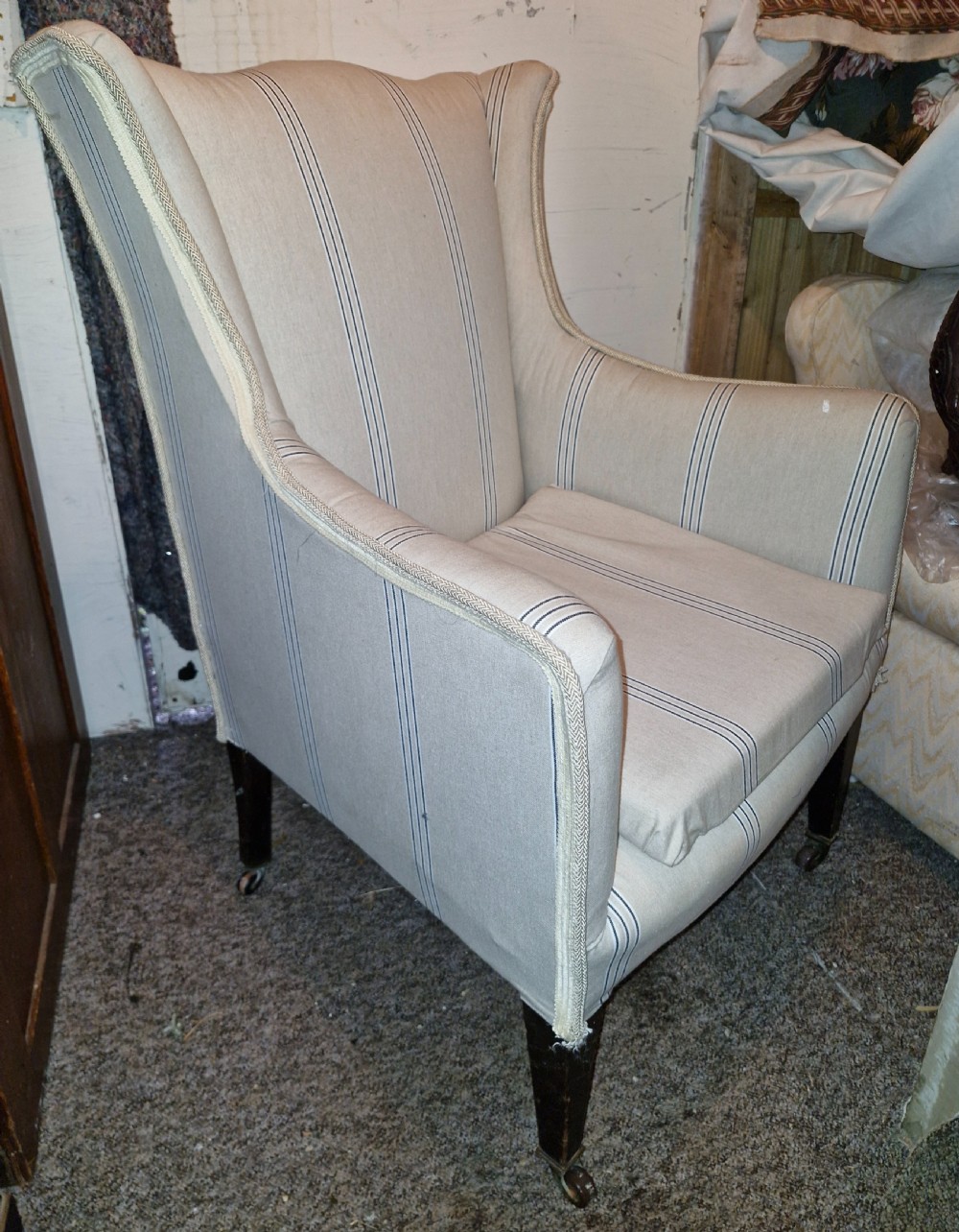 An Edwardian upholstered bedroom armchair covered in beige ticking stripe linen with tapered front legs set on brass castors. View VI
