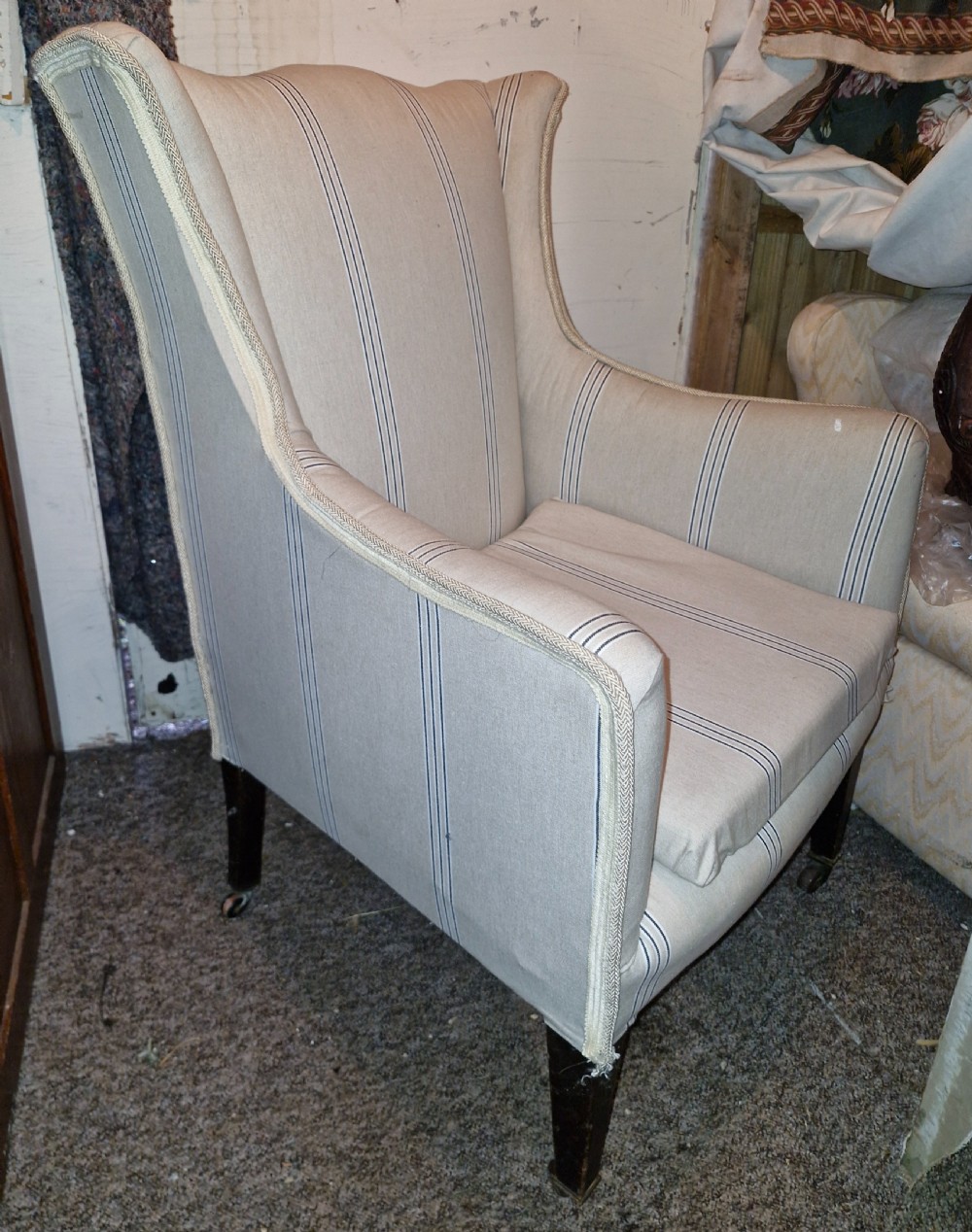An Edwardian upholstered bedroom armchair covered in beige ticking stripe linen with tapered front legs set on brass castors. View VII