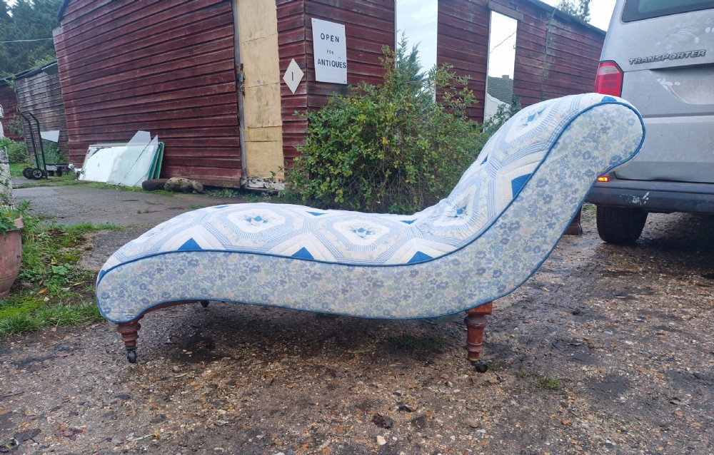 A late Victorian upholstered day bed with an S-shaped contour, blue and white patterned fabric, turned timber legs, and small wheel castors.