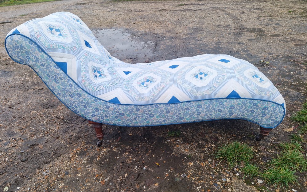 A late Victorian upholstered day bed with an S-shaped contour, blue and white patterned fabric, turned timber legs, and small wheel castors. View IV