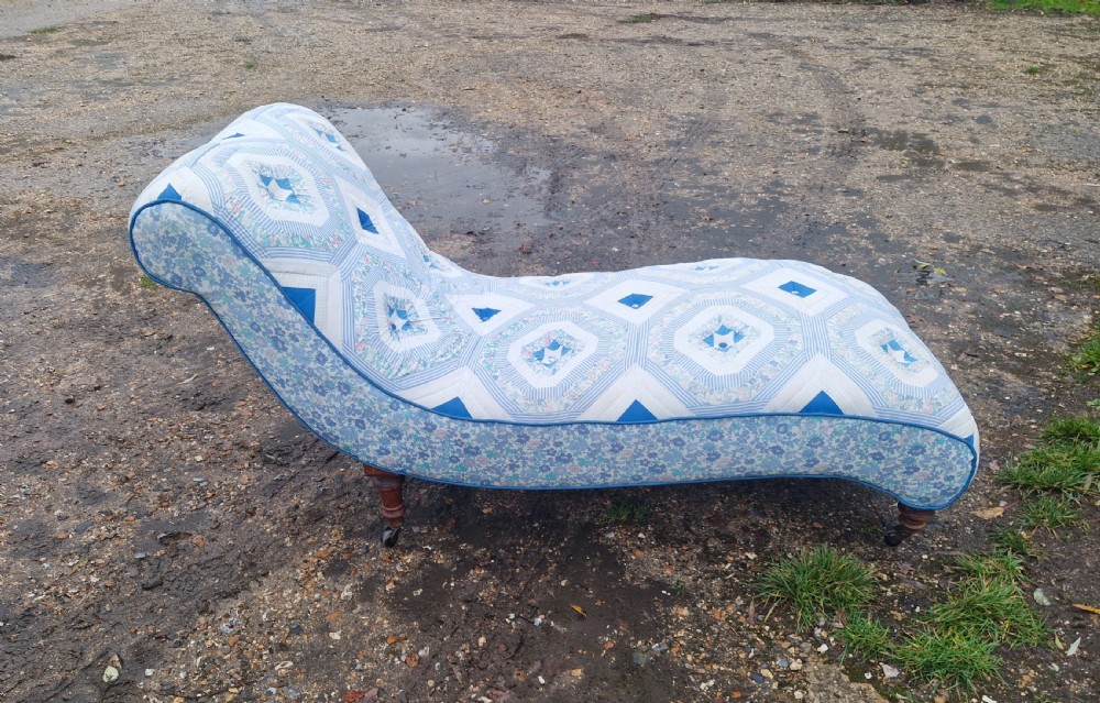 A late Victorian upholstered day bed with an S-shaped contour, blue and white patterned fabric, turned timber legs, and small wheel castors. View V