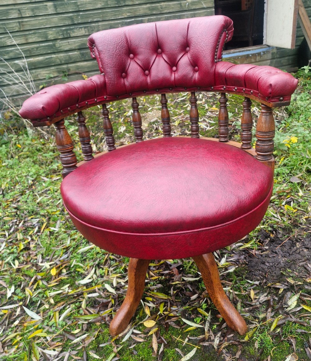A late Victorian oak revolving desk armchair featuring deep button-tufted red upholstery, turned spindle back supports, and a four-point splayed wooden base.