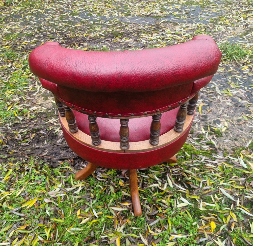 A late Victorian oak revolving desk armchair featuring deep button-tufted red upholstery, turned spindle back supports, and a four-point splayed wooden base. View III