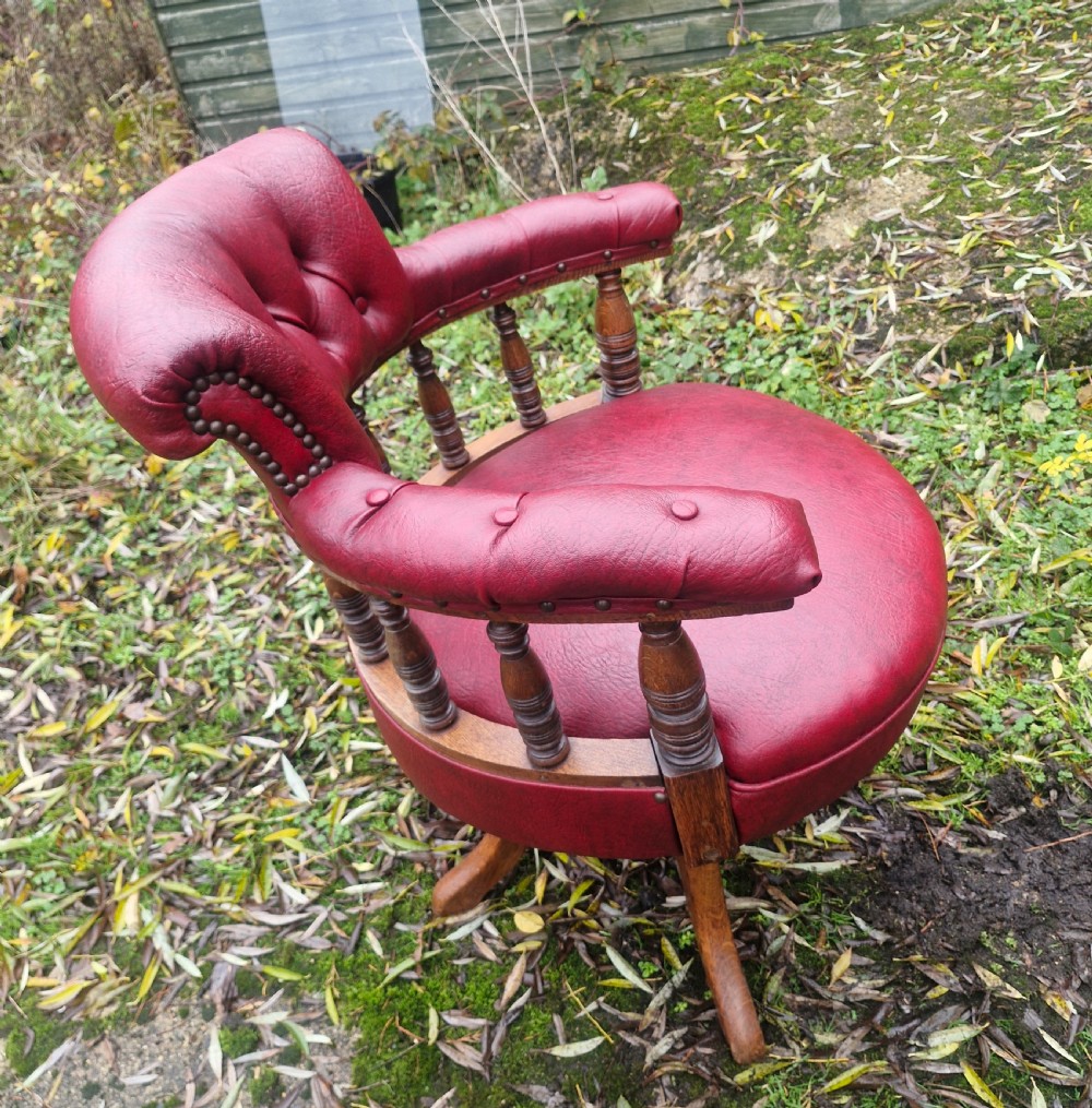 A late Victorian oak revolving desk armchair featuring deep button-tufted red upholstery, turned spindle back supports, and a four-point splayed wooden base. View IV