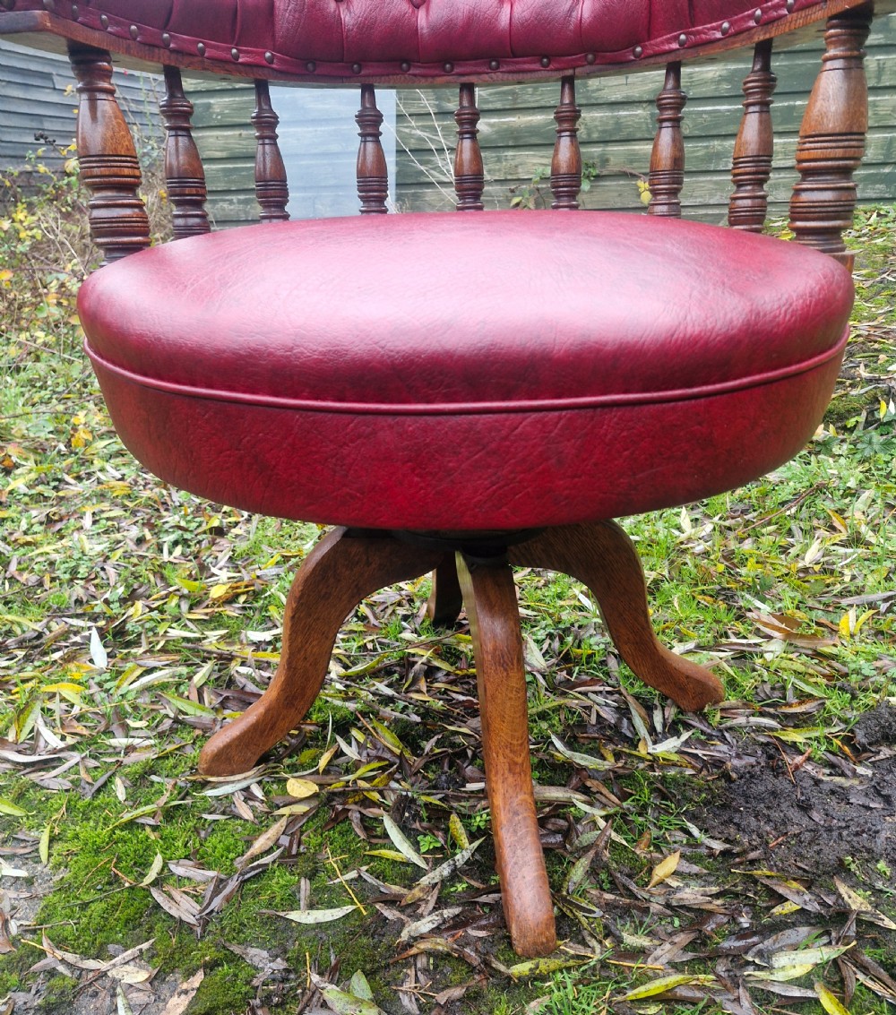 A late Victorian oak revolving desk armchair featuring deep button-tufted red upholstery, turned spindle back supports, and a four-point splayed wooden base. View V