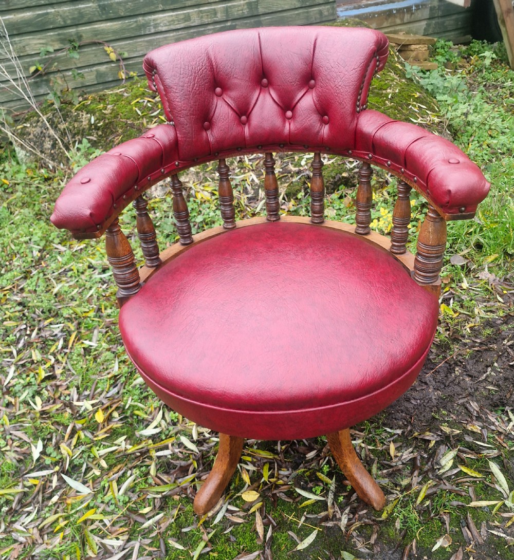 A late Victorian oak revolving desk armchair featuring deep button-tufted red upholstery, turned spindle back supports, and a four-point splayed wooden base. View VII