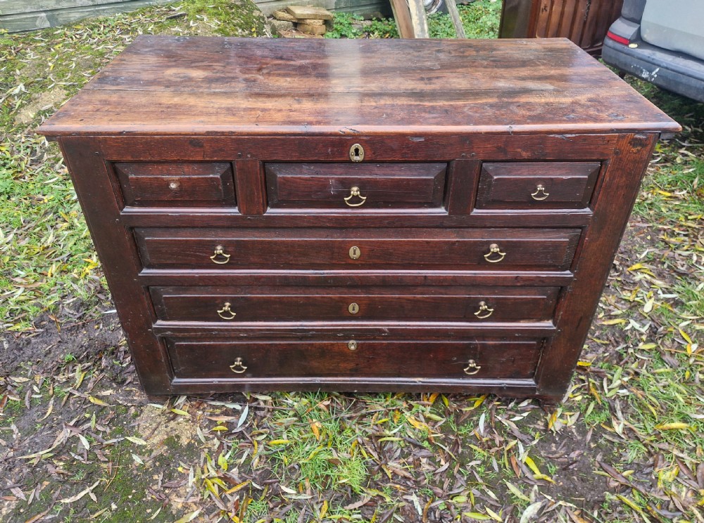 A dark brown Georgian oak chest of drawers featuring geometric moulded drawer fronts and brass drop handles.