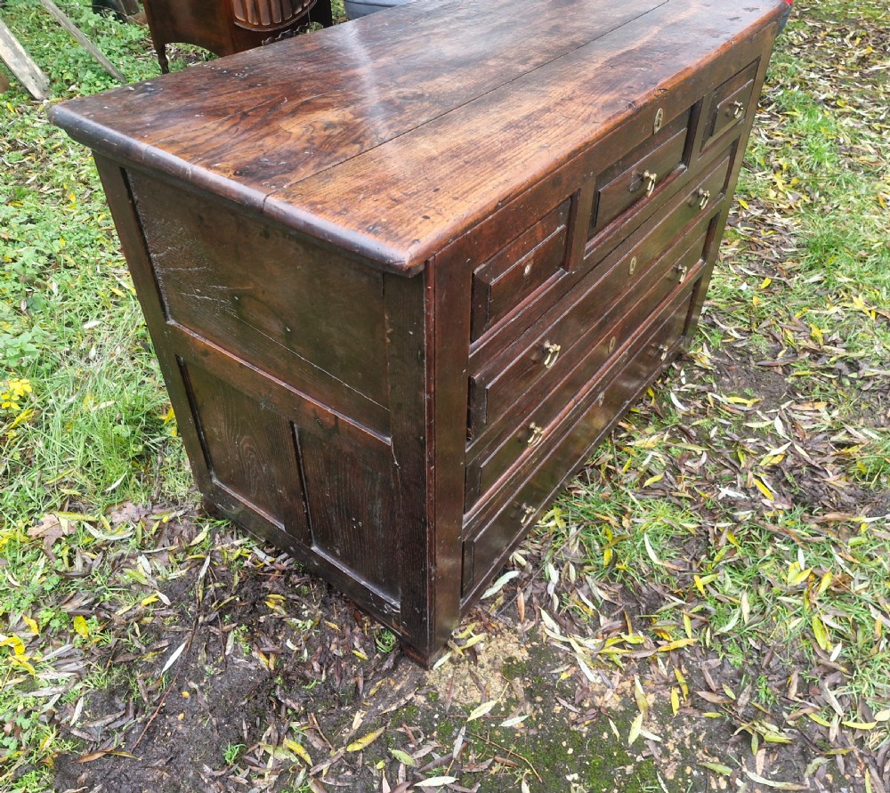 A dark brown Georgian oak chest of drawers featuring geometric moulded drawer fronts and brass drop handles. View V