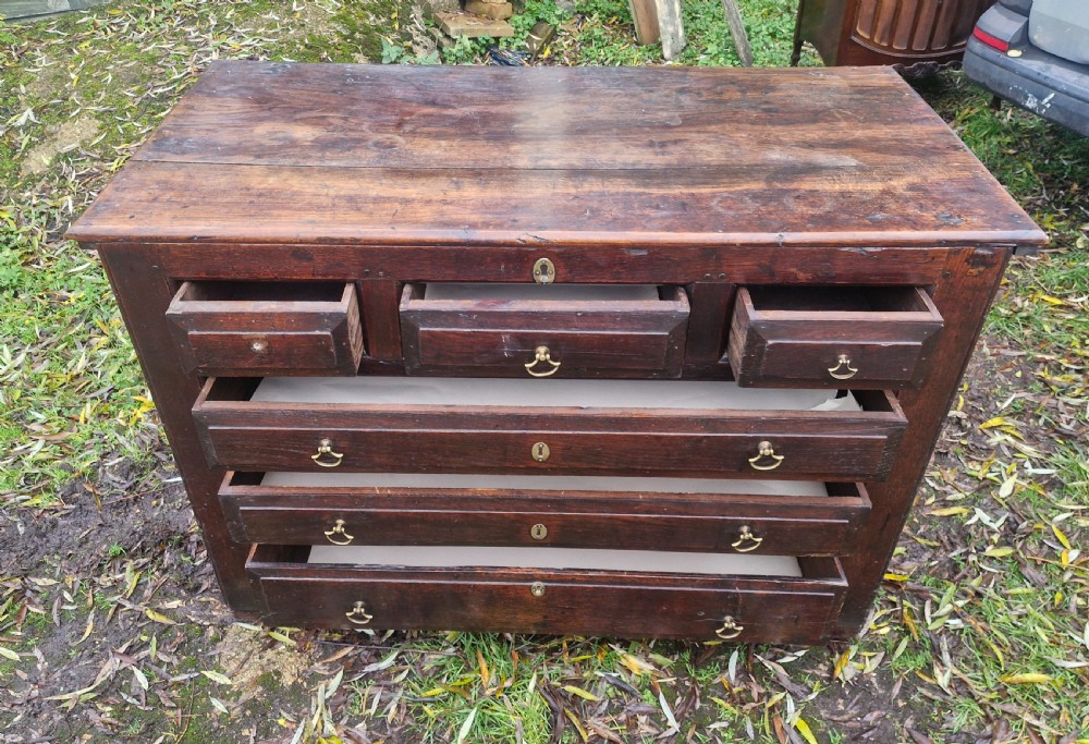 A dark brown Georgian oak chest of drawers featuring geometric moulded drawer fronts and brass drop handles. View IX