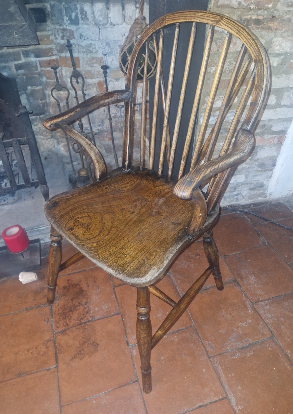A 19th-century dark wooden Windsor armchair featuring a curved stick back, sculpted seat, curved armrests, and turned legs.