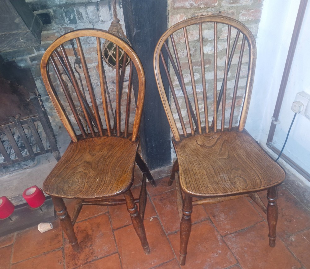 A pair of Victorian stick back Windsor kitchen chairs crafted from timber with contoured seats and turned front legs.