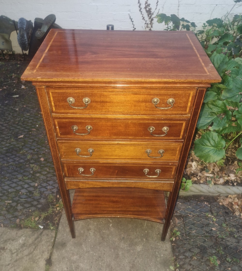An Edwardian mahogany music cabinet featuring four drop-down drawers with brass handles, satinwood stringing inlay, and a low open shelf.