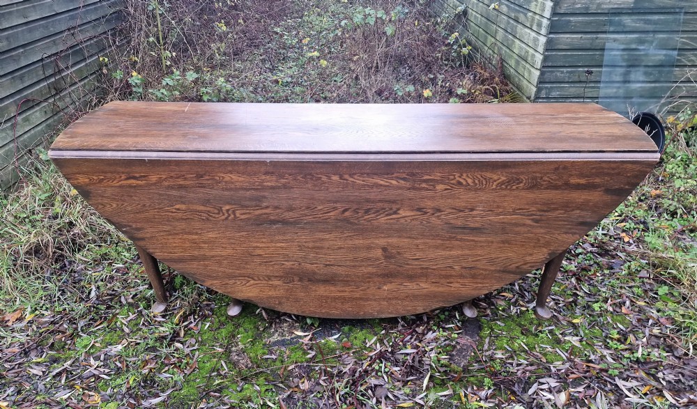 A large dark oak gateleg dining table with both rounded drop-leaf sides folded downward.