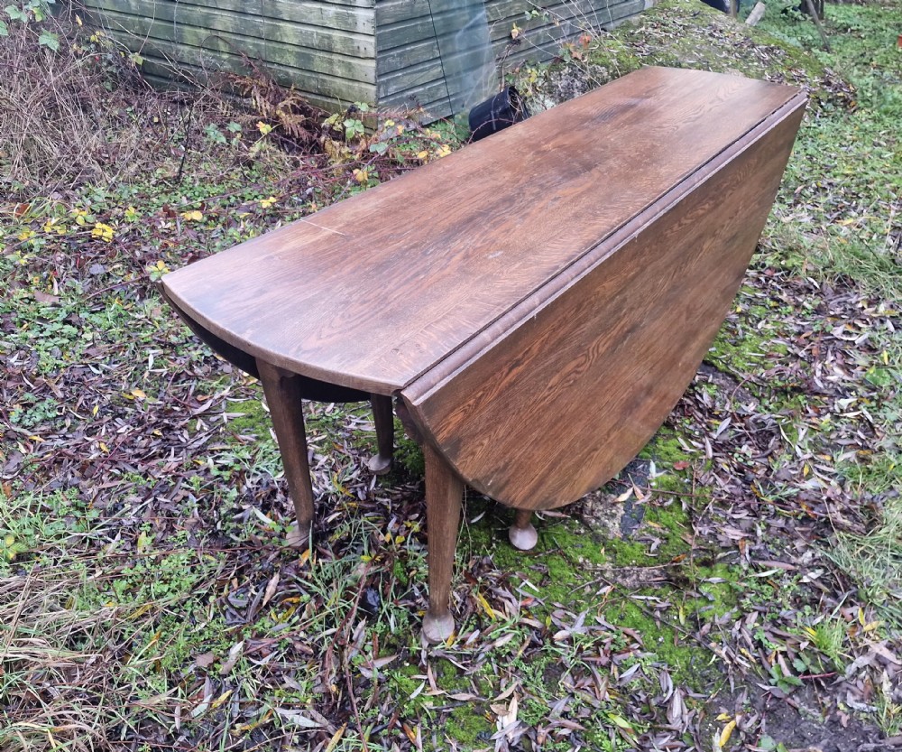 A large dark oak gateleg dining table with both rounded drop-leaf sides folded downward. View II