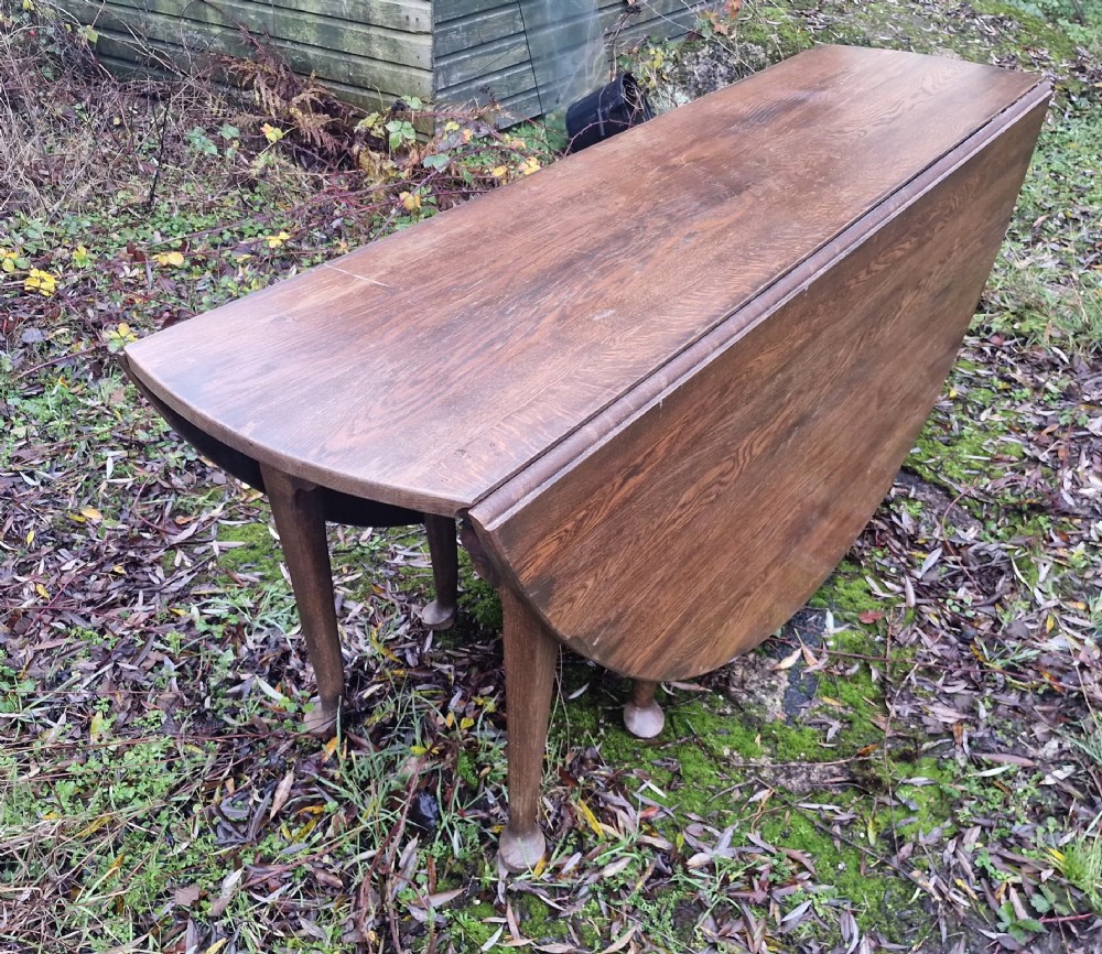 A large dark oak gateleg dining table with both rounded drop-leaf sides folded downward. View III