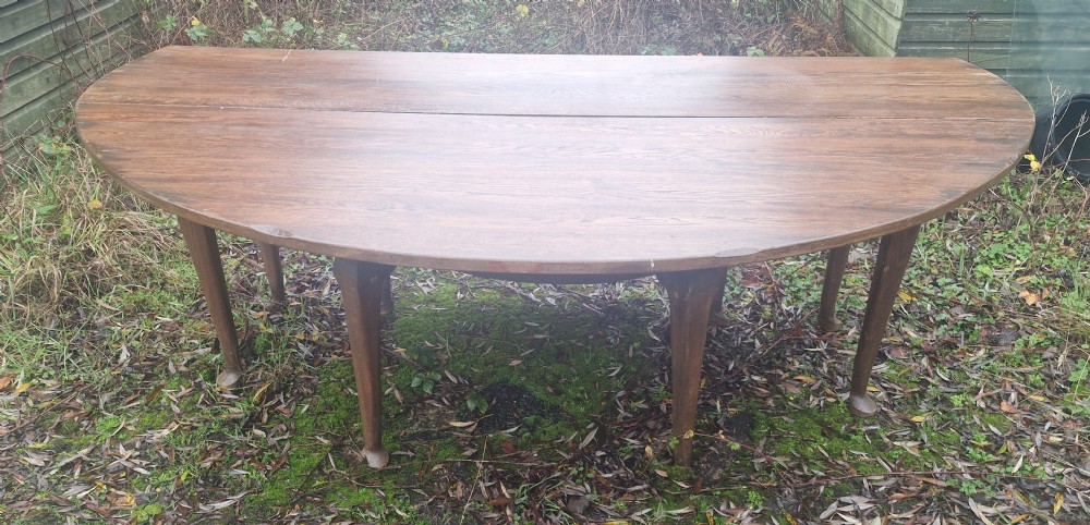 A large dark oak gateleg dining table with both rounded drop-leaf sides folded downward. View IV