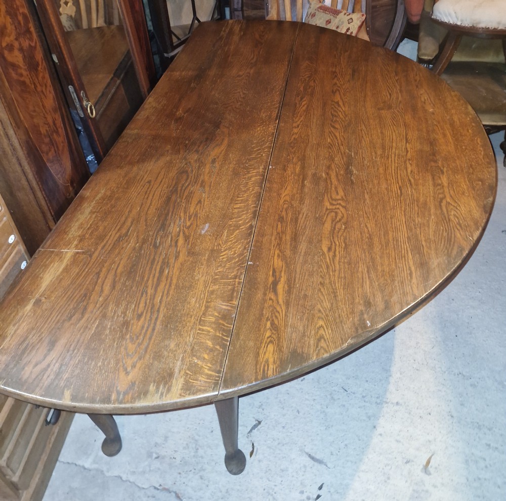A large dark oak gateleg dining table with both rounded drop-leaf sides folded downward. View V