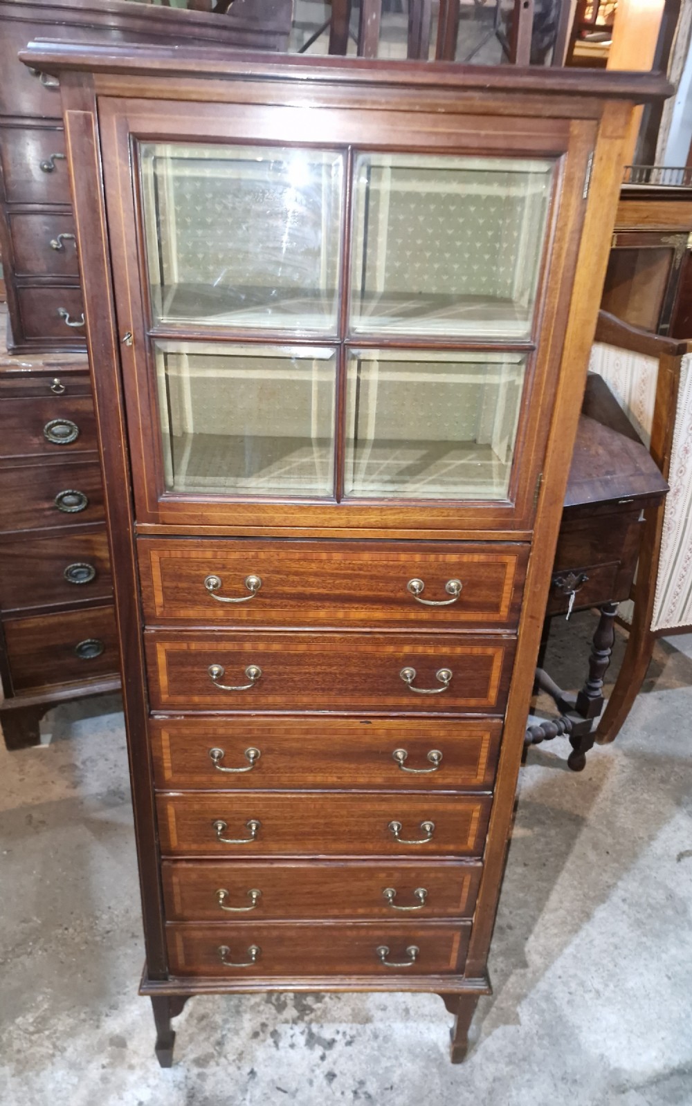 An Edwardian mahogany music cabinet featuring a four-pane glazed upper door above six inlaid drawers with brass drop handles. View IV