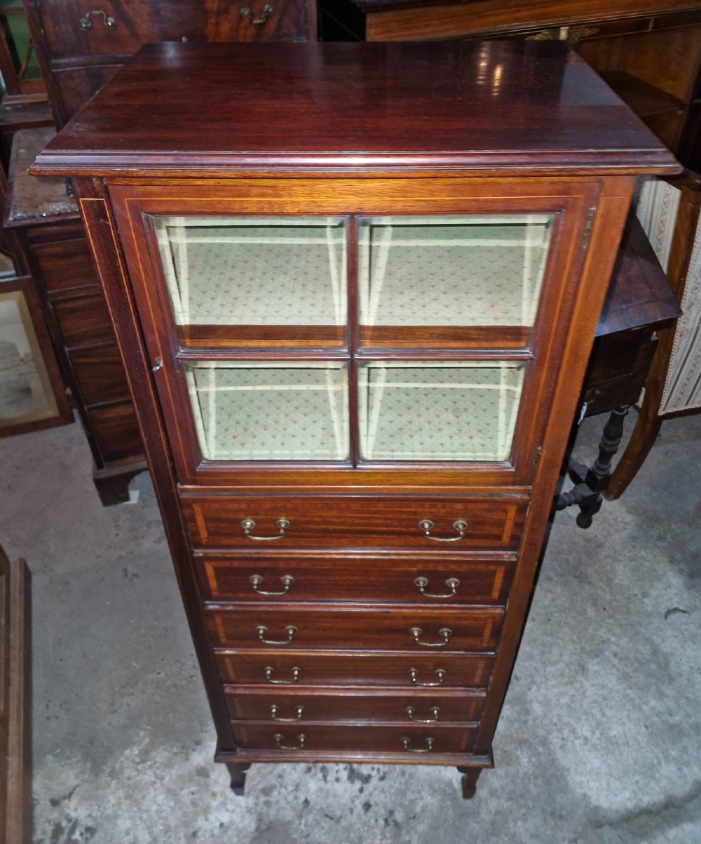 An Edwardian mahogany music cabinet featuring a four-pane glazed upper door above six inlaid drawers with brass drop handles. View V