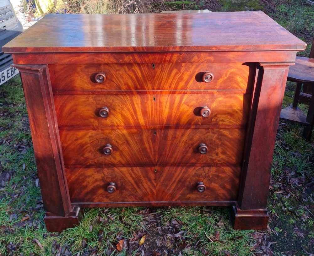 A nineteenth-century Regency chest of drawers featuring four graduated drawers with flame mahogany veneers, turned wooden knobs, and flanking side pilasters.