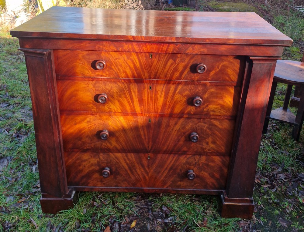 A nineteenth-century Regency chest of drawers featuring four graduated drawers with flame mahogany veneers, turned wooden knobs, and flanking side pilasters. View IV
