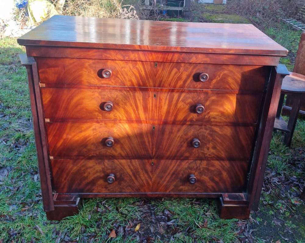 A nineteenth-century Regency chest of drawers featuring four graduated drawers with flame mahogany veneers, turned wooden knobs, and flanking side pilasters. View V