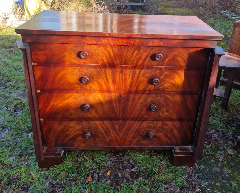 A nineteenth-century Regency chest of drawers featuring four graduated drawers with flame mahogany veneers, turned wooden knobs, and flanking side pilasters. View VI