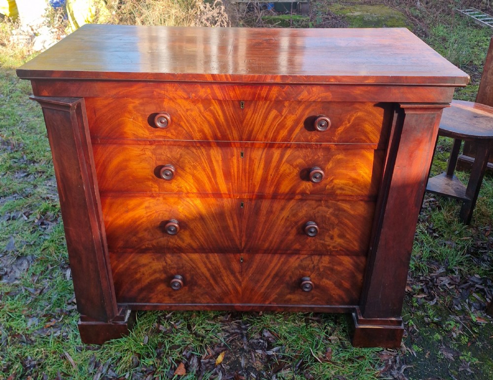 A nineteenth-century Regency chest of drawers featuring four graduated drawers with flame mahogany veneers, turned wooden knobs, and flanking side pilasters. View VII