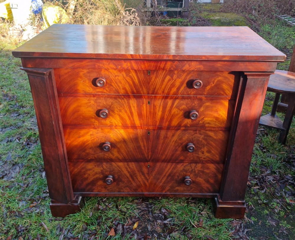 A nineteenth-century Regency chest of drawers featuring four graduated drawers with flame mahogany veneers, turned wooden knobs, and flanking side pilasters. View VIII