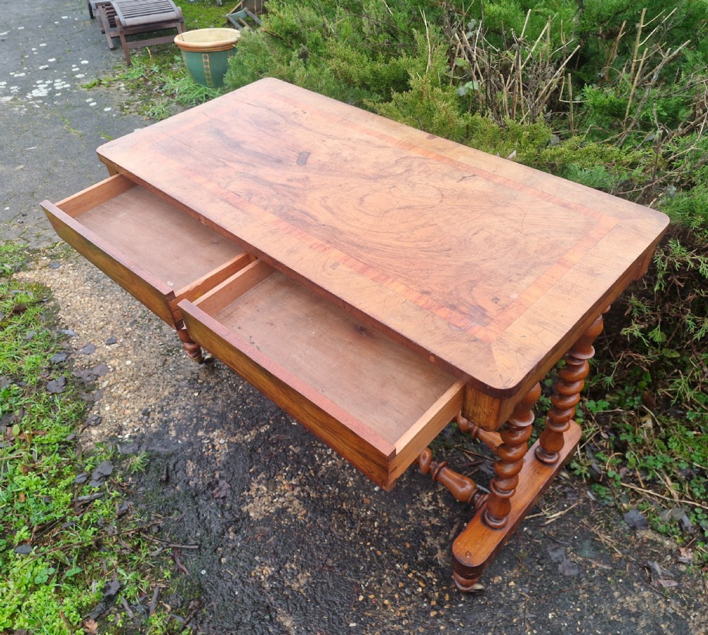 A Victorian walnut side table featuring a rectangular inlaid top, two frieze drawers, and turned barley twist legs connected by stretchers on brass castors. View II