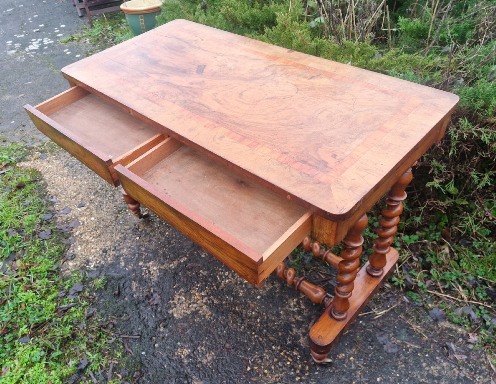 A Victorian walnut side table featuring a rectangular inlaid top, two frieze drawers, and turned barley twist legs connected by stretchers on brass castors. View IV