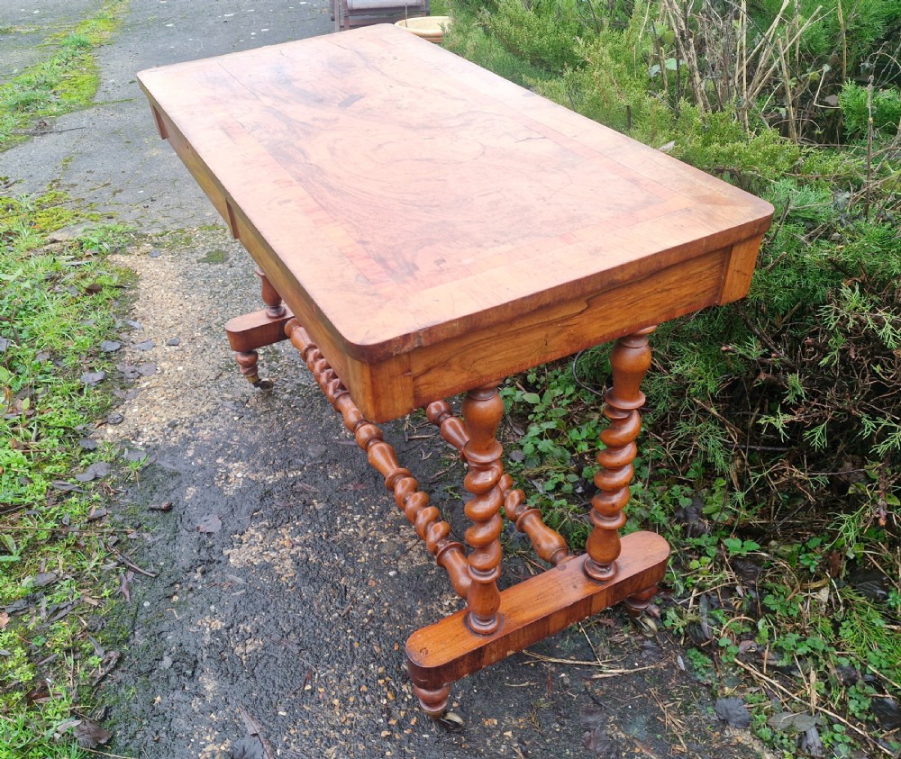 A Victorian walnut side table featuring a rectangular inlaid top, two frieze drawers, and turned barley twist legs connected by stretchers on brass castors. View VI