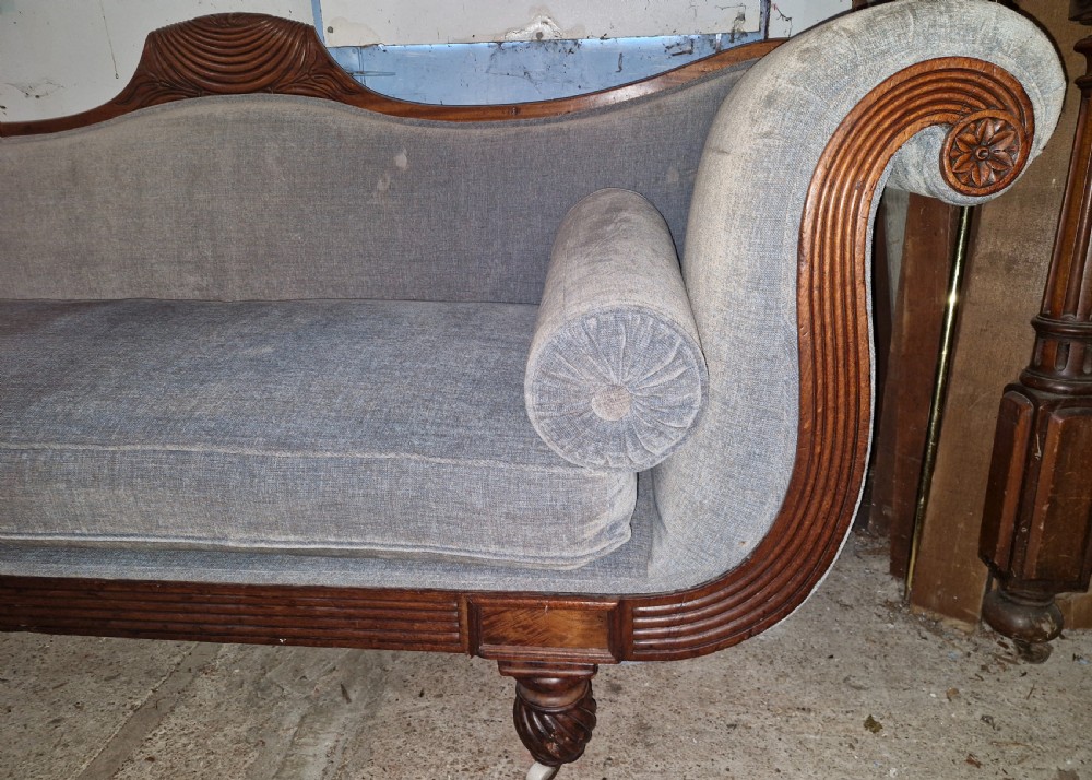 A Regency period mahogany hall sofa upholstered in grey fabric with scrolled ends, reeded frame details, shell cresting, turned spiralled feet on castors, and two cylindrical bolster cushions. View V