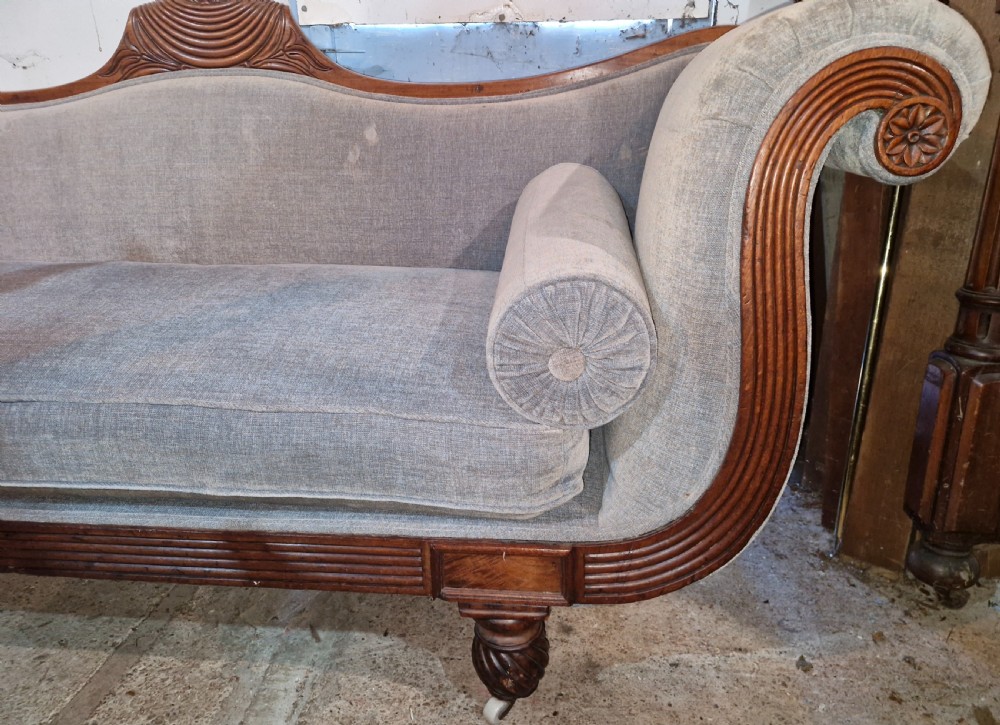 A Regency period mahogany hall sofa upholstered in grey fabric with scrolled ends, reeded frame details, shell cresting, turned spiralled feet on castors, and two cylindrical bolster cushions. View VI