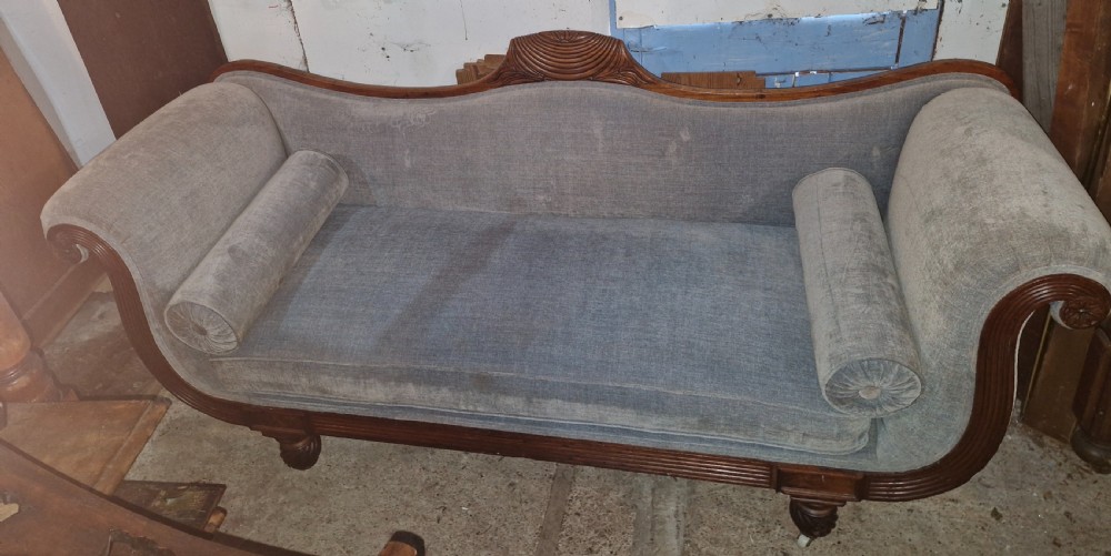 A Regency period mahogany hall sofa upholstered in grey fabric with scrolled ends, reeded frame details, shell cresting, turned spiralled feet on castors, and two cylindrical bolster cushions. View VII
