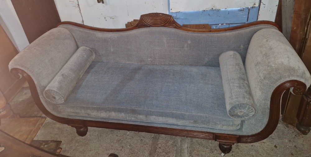 A Regency period mahogany hall sofa upholstered in grey fabric with scrolled ends, reeded frame details, shell cresting, turned spiralled feet on castors, and two cylindrical bolster cushions. View VIII