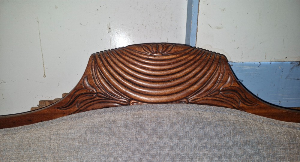 A Regency period mahogany hall sofa upholstered in grey fabric with scrolled ends, reeded frame details, shell cresting, turned spiralled feet on castors, and two cylindrical bolster cushions. View X