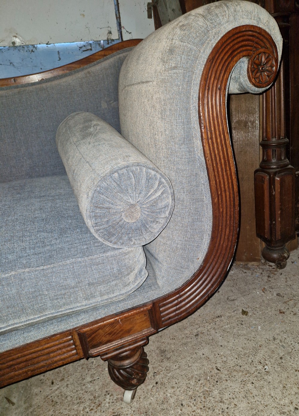 A Regency period mahogany hall sofa upholstered in grey fabric with scrolled ends, reeded frame details, shell cresting, turned spiralled feet on castors, and two cylindrical bolster cushions. View XI