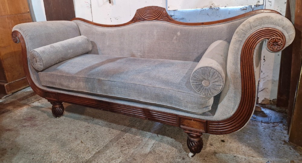 A Regency period mahogany hall sofa upholstered in grey fabric with scrolled ends, reeded frame details, shell cresting, turned spiralled feet on castors, and two cylindrical bolster cushions. View XII