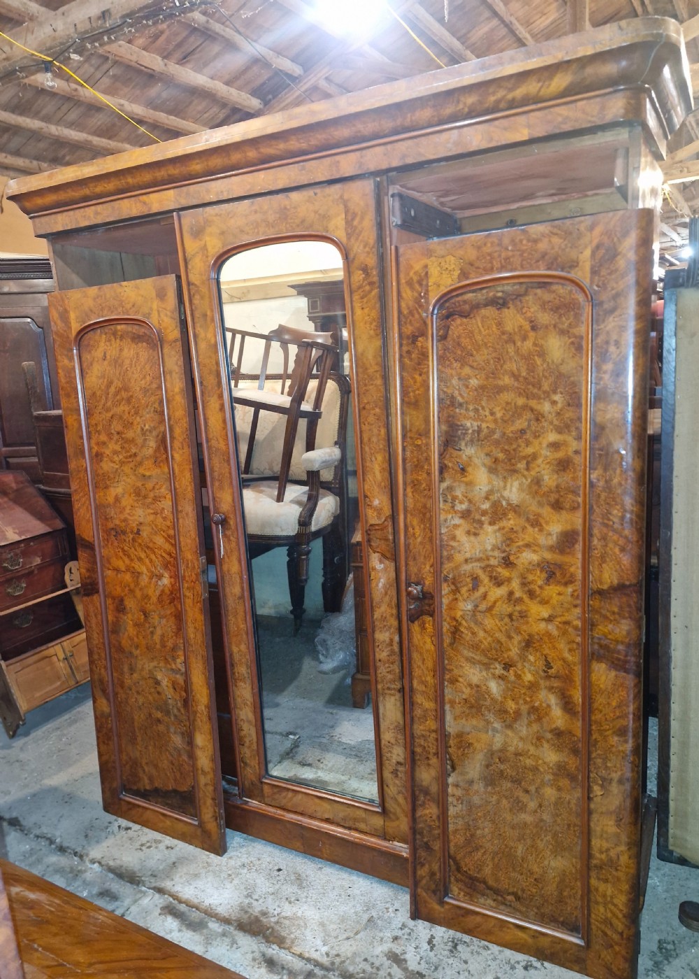 A nineteenth-century Victorian triple wardrobe crafted from figured burr walnut, featuring a central mirrored door flanked by two panelled timber doors.