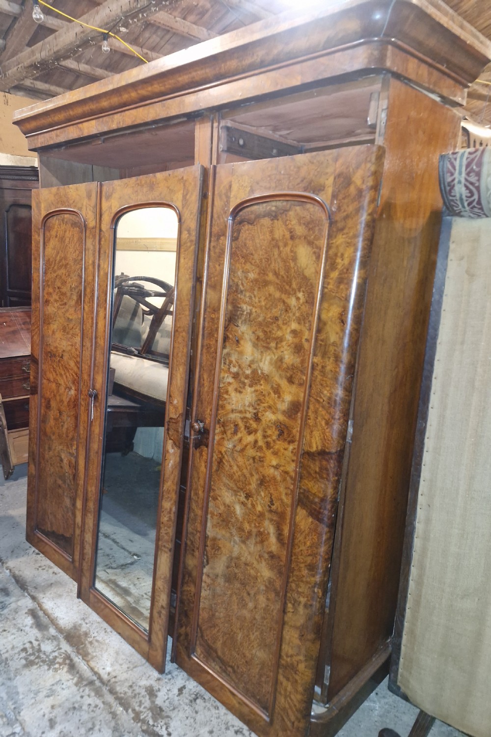 A nineteenth-century Victorian triple wardrobe crafted from figured burr walnut, featuring a central mirrored door flanked by two panelled timber doors. View IX
