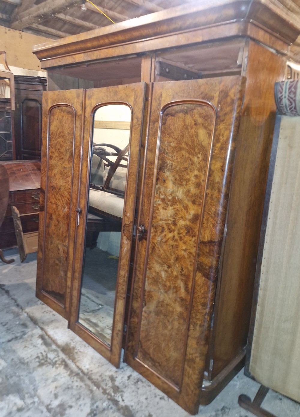A nineteenth-century Victorian triple wardrobe crafted from figured burr walnut, featuring a central mirrored door flanked by two panelled timber doors. View X