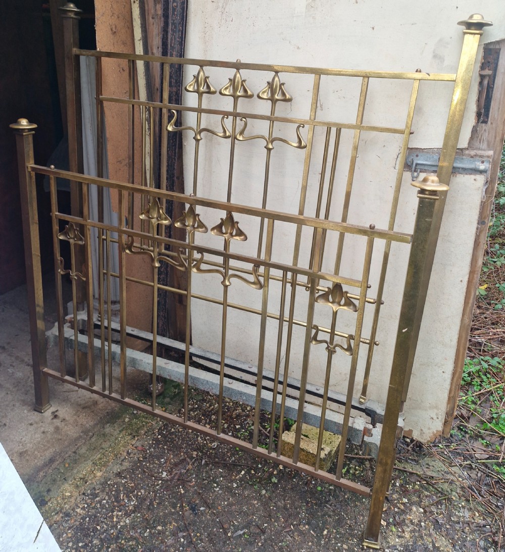 An Art Nouveau brass double bed frame with headboard, footboard, and original side irons featuring stylized floral motifs.