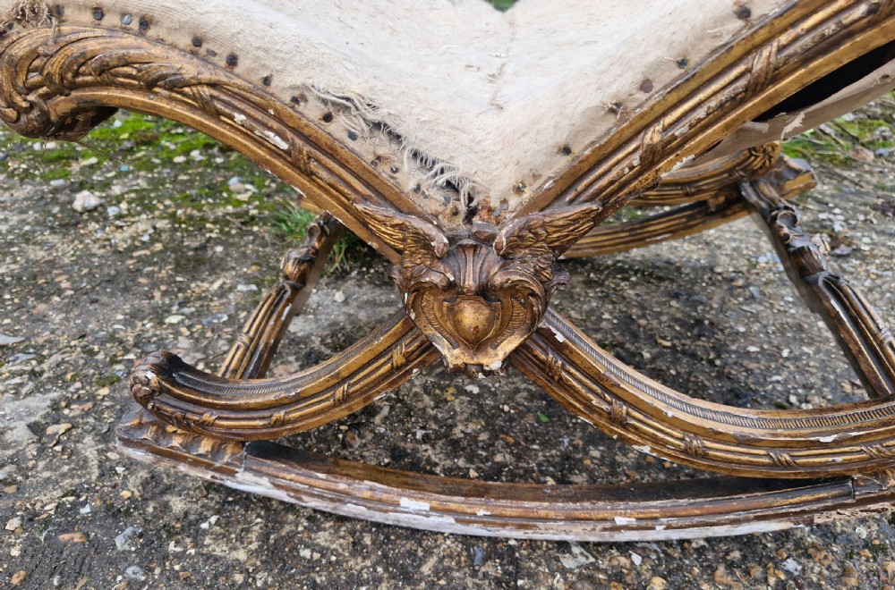 A late 19th-century giltwood rocking gout stool featuring a deeply curved cream fabric-upholstered seat supported by an ornate carved gilded frame. View II
