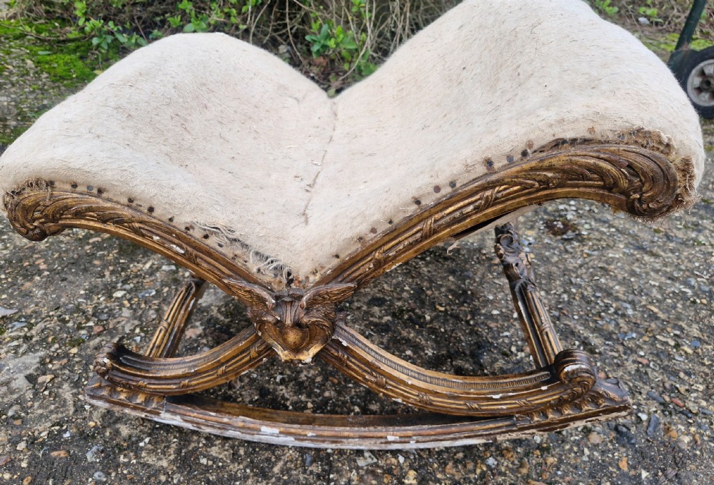 A late 19th-century giltwood rocking gout stool featuring a deeply curved cream fabric-upholstered seat supported by an ornate carved gilded frame. View III
